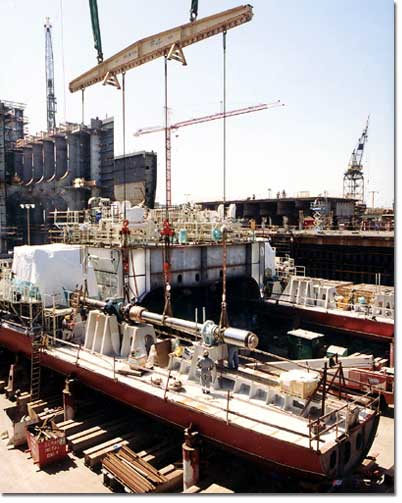 A crane places one of two drive shafts for the ship's&nbsp;twin-screw, diesel-electric propulsion plant. Environmental safety and redundancy will be implemented by segregating the propulsion systems in separate engine rooms, with four engines driving two propellers and twin rudders.