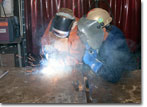 The honoree, Mrs. Gina Buzby, wife of Admiral Buzby, writes out her initials with welding material.