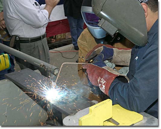Mrs. Debbie Hamilton, wife of RADM Charies Hamilton, practices welding her initials onto a keel plate.