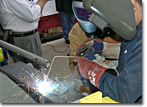Mrs. Debbie Hamilton, wife of RADM Charies Hamilton, practices welding her initials onto a keel plate.
