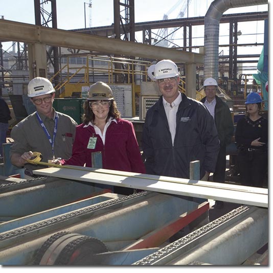 Mrs. Catherine Cunningham observes the measurement of the first steel component cut for T-AKE 6.