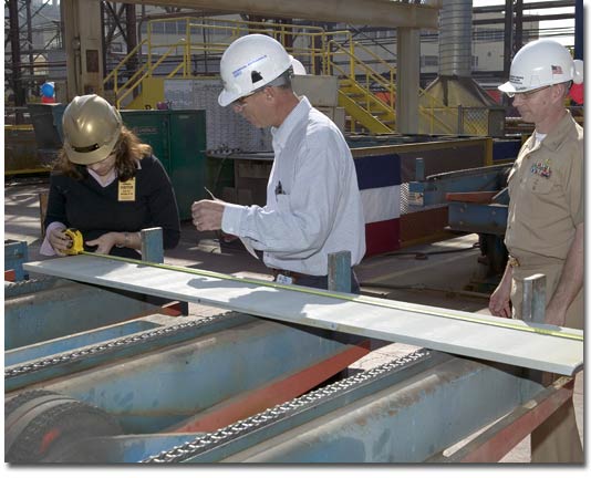 Mrs. Crowe inspects the steel part she cut for T-AKE 8, as NASSCO's Manager of Steel Gene Martinelli and her husband, CDR Rob Crowe, look on.