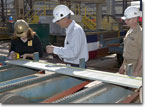 Mrs. Crowe inspects the steel part she cut for T-AKE 8, as NASSCO's Manager of Steel Gene Martinelli and her husband, CDR Rob Crowe, look on.